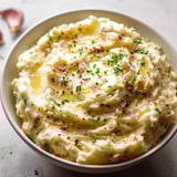 Eine Schale mit Kartoffelbrei, garniert mit grünen Kräutern.