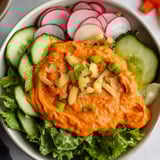 Eine Schüssel Salat mit roter Soße und geschnittenem Gemüse.