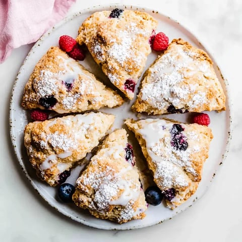 Ein Teller mit frisch gebackenen Scones, bestäubt mit Puderzucker und garniert mit Himbeeren und Heidelbeeren.
