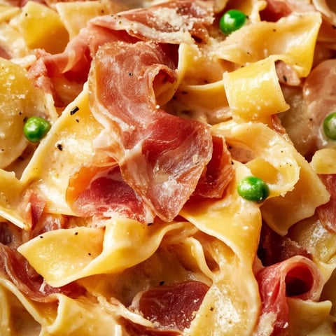 Ein Teller Pasta mit Schinken und Erbsen.